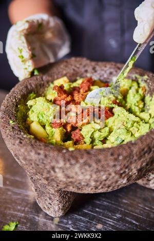 Guacamole authentique à Molcajete avec Bacon bits - préparation des aliments en gros plan Banque D'Images