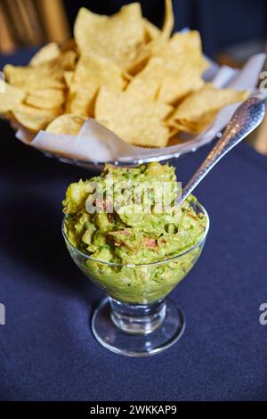 Guacamole frais dans une tasse en verre avec des chips de tortilla sur nappe bleue Banque D'Images