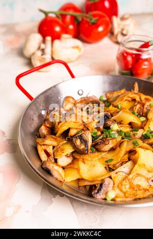 Pommes de terre tranchées, champignons frais et oignons en dés grésillant dans une poêle sur fond blanc propre, prêts à être cuits. Banque D'Images