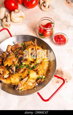 Pommes de terre tranchées, champignons frais et oignons en dés grésillant dans une poêle sur fond blanc propre, prêts à être cuits. Banque D'Images