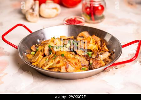 Pommes de terre tranchées, champignons frais et oignons en dés grésillant dans une poêle sur fond blanc propre, prêts à être cuits. Banque D'Images