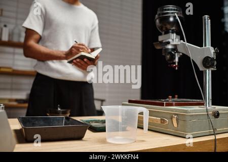 plateau de film et d'autres équipements de développement photographique près de l'homme noir avec cahier dans une chambre noire Banque D'Images