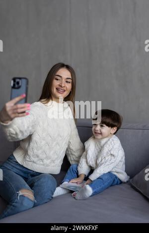 Maman et enfant en bas âge prenant selfie dans un salon confortable Banque D'Images