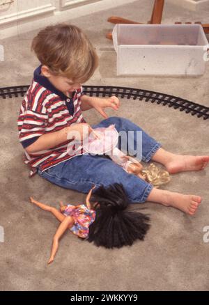 Un garçon de trois ans joue avec des poupées Barbie à la maison. ©Bob Daemmrich Banque D'Images