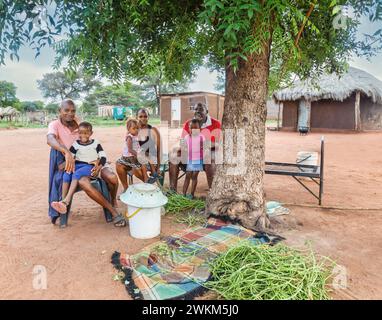 village heureux étendu multigénération famille africaine, assis sur des chaises dans la cuisine extérieure, en face de la cabane de boue avec toit de chaume Banque D'Images