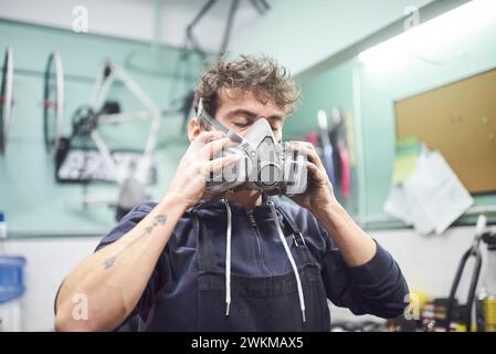 Jeune travailleur latin enlevant un masque de protection respiratoire, alors qu'il termine un travail de peinture au pistolet dans son atelier. Protection de la santé dans l'industrie Banque D'Images