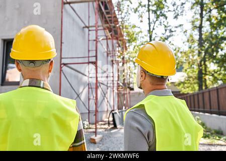 vue arrière des constructeurs de chalets dans des casques de sécurité regardant les échafaudages sur le chantier de construction Banque D'Images