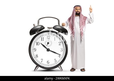 Homme arabe saoudien avec un grand réveil pointant vers le haut isolé sur fond blanc Banque D'Images