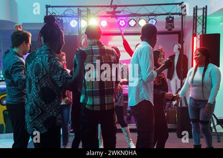 Les jeunes appréciant le concert sur dancefloor avec des projecteurs pendant la performance de musique live dans la boîte de nuit. Les gens se bousculent et dansent tout en assistant à la fête la nuit Banque D'Images