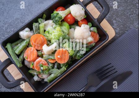 légumes surgelés mélangés. Les légumes congelés dans une poêle en fonte sont préparés pour la cuisson. Mélange de carottes finement hachées, chou-fleur, brocoli et Banque D'Images