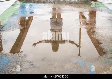 Réflexion d'une personne non identifiée dans la flaque d'eau sur le sol en ciment. Photo abstraite, arrière-plan et texture. Banque D'Images