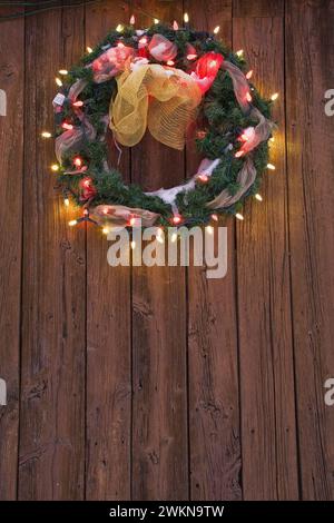 Gros plan de la couronne de Noël illuminée sur le mur de planche en bois du hangar de stockage au crépuscule en hiver. Banque D'Images