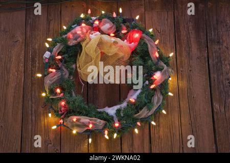 Gros plan de la couronne de Noël illuminée sur le mur de planche en bois du hangar de stockage au crépuscule en hiver. Banque D'Images