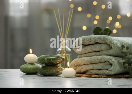 Composition pour spa. Serviettes, pierres, désodorisant roseau et bougies allumées sur la table en marbre blanc contre les lumières floues Banque D'Images