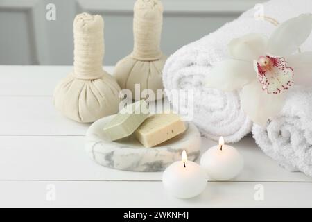 Belle composition de spa. Serviettes, sacs à base de plantes, barres de savon et bougies allumées sur la table en bois blanc Banque D'Images