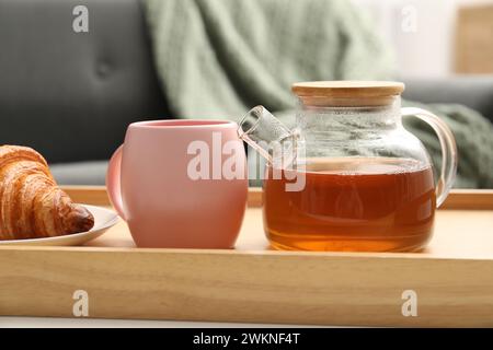 Thé aromatique en théière, tasse et croissant savoureux sur table à l'intérieur Banque D'Images