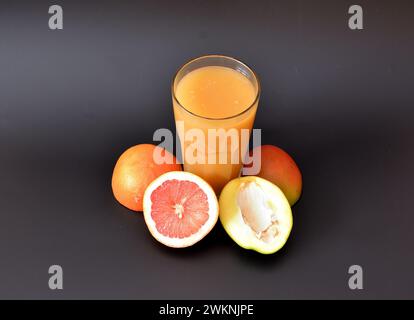 Un grand verre à facettes d'un mélange de fruits tropicaux sur un fond noir, à côté des moitiés d'un pamplemousse mûr et pitaya. Gros plan. Banque D'Images