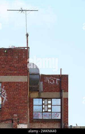 Ancien bâtiment en briques rouges abandonné avec graffiti et fenêtres, fond de ciel bleu clair, Melbourne, Australie. Banque D'Images