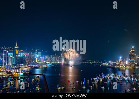 Des feux d'artifice éclatent dans le ciel nocturne au-dessus de la ligne d'horizon de la ville, se reflétant dans l'eau calme en contrebas Banque D'Images
