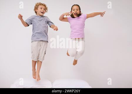 Saut, lit et enfants avec plaisir, énergie et matin dans une chambre avec jeu et frère. Jeunesse, hop et maison avec un enfant excité sur une couette en air Banque D'Images