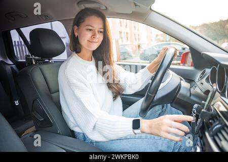 Jeune femme conduisant une voiture et utilisant l'application smartphone pour afficher une carte montrant l'itinéraire de voyage Banque D'Images
