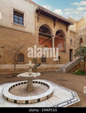 La cour sereine met en valeur la beauté intemporelle de l'architecture mamelouk avec de grandes arches et des pierres avec escalier accueillant menant à un balcon orné. Une fontaine de marbre classique se trouve au centre Banque D'Images