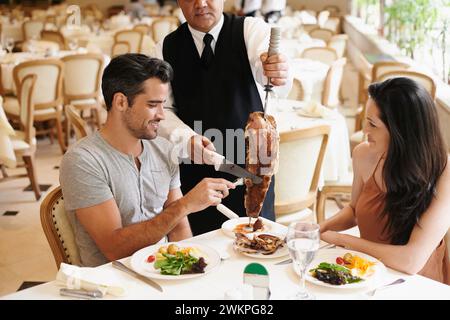 Couple heureux, date et dîner avec kebab de serveur servant, viande ou tranches sur le dîner romantique à table. Jeune homme ou femme avec chef, brochette ou nourriture Banque D'Images