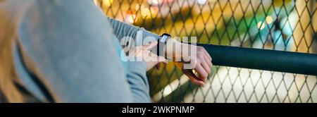 Bannière de main féminine méconnaissable touchant l'écran de bracelet numérique pour vérifier le compteur de pas quotidien après avoir marché la nuit sur la ville. Look athlète féminin Banque D'Images