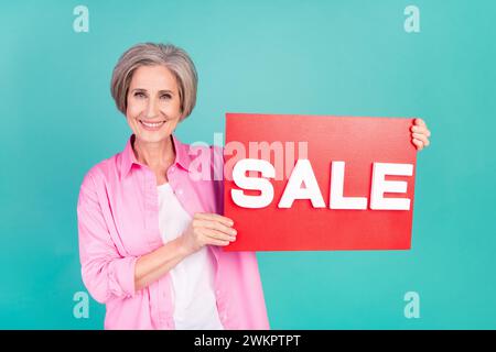 Photo de promoteur femme âgée habillée rose chemise à la mode promouvant la vente dans le magasin local avec placard d'annonce isolé sur fond de couleur bleue Banque D'Images