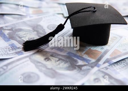 Chapeau de graduation sur une pile de billets de cent dollars US. Financement de l'éducation, concept de prêt étudiant. Banque D'Images