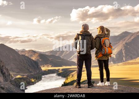 Jeune couple de touristes est debout avec des sacs à dos dans les montagnes et bénéficie d'une belle vue au coucher du soleil et grande rivière Banque D'Images