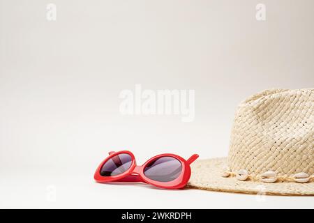 Lunettes de soleil rouges et chapeau de paille placés sur un fond neutre Banque D'Images
