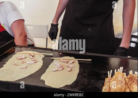 Crêpes d'un boulanger professionnel dans la rue. Cuisson des crêpes de poulet dans une poêle chaude à la vapeur. Banque D'Images