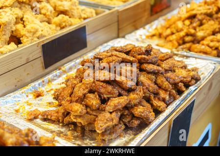 Généreuses portions d'ailes de poulet glacées au miel, brillantes et parfaitement cuites, exposées sur un étal de marché alimentaire Banque D'Images