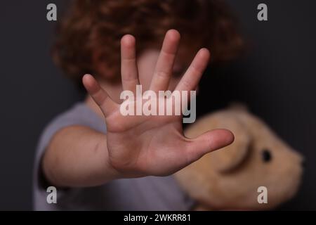 Maltraitance des enfants. Garçon avec jouet faisant un geste d'arrêt près du mur gris, mise au point sélective Banque D'Images