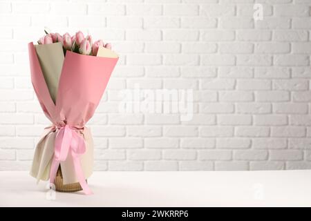 Beau bouquet de tulipes roses fraîches sur la table près du mur de briques blanches. Espace pour le texte Banque D'Images