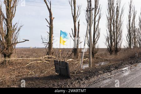 DONETSK REG., UKRAINE - 14 février 2024 : guerre en Ukraine. Un drapeau déchiré mais fièrement flottant est vu le long d'une route dans la région de Donetsk, symbole d'une Ukraine libre invincible. Banque D'Images