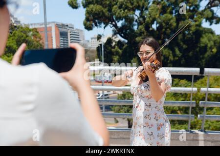 Femme méconnaissable filme avec son téléphone busker femme violoniste en plein air tout en jouant du violon et en faisant de la musique de rue, concept de technologie, copie Banque D'Images