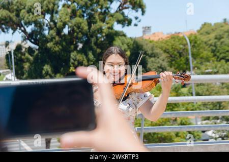 Femme méconnaissable filme avec son téléphone busker femme violoniste en plein air tout en jouant du violon et en faisant de la musique de rue, concept de technologie, copie Banque D'Images