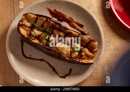 Une aubergine farcie de fromage et de sauce barbecue sur une assiette grise et le fond légèrement flou également dans des tons neutres Banque D'Images