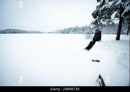 Voyageur randonneur se reposer et boire du café chaud ou du thé au bord du lac enneigé dans la forêt d'hiver, actif en plein air voyageant Banque D'Images