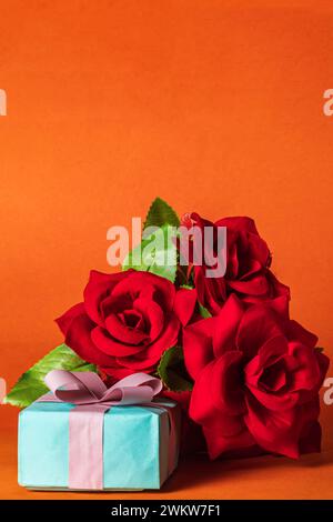 Bouquet de roses rouges et boîte cadeau sur fond orange. Saint-Valentin. Banque D'Images