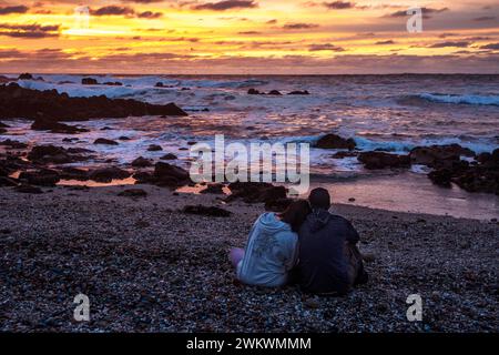 Couple sitting on beach at sunset Banque D'Images