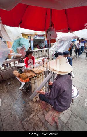 Un homme à un étal de vendeurs de tabac dans un marché chinois du Yunnan fumant une pipe commerciale. Banque D'Images