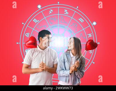 Portrait de jeune couple avec des ballons en forme de coeur et des signes dessinés du zodiaque sur fond rouge. Horoscope de compatibilité d'amour. Mise en correspondance des partenaires par date o Banque D'Images