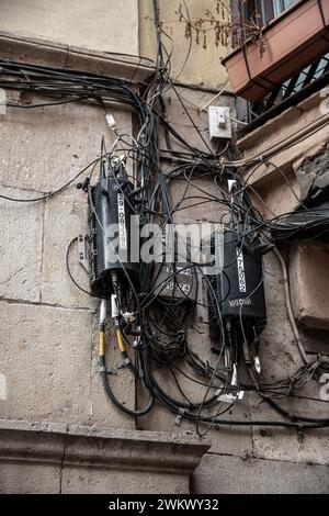 Beaucoup de câbles téléphoniques noirs sur un mur de maison, qui finissent par être désorganisés et emmêlés dans des boîtes de jonction. Certains câbles sont étiquetés. C'est une challe Banque D'Images