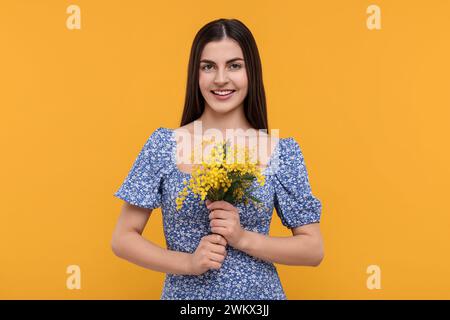 Heureuse jeune femme avec beau bouquet sur fond orange Banque D'Images