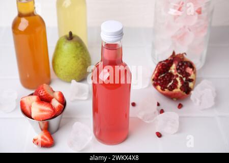 Savoureux kombucha dans des bouteilles en verre, des fruits frais et de la glace sur une table carrelée blanche Banque D'Images