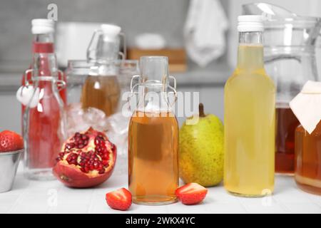 Savoureux kombucha dans des bouteilles en verre et fruits frais sur une table carrelée blanche Banque D'Images