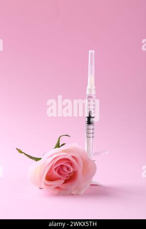 Cosmétologie. Seringue médicale et fleur de rose sur fond rose Banque D'Images